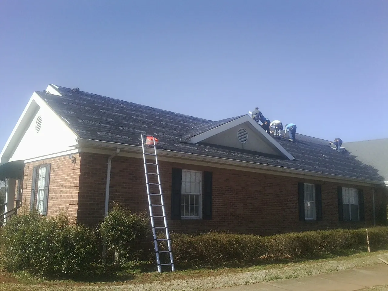 Crew tearing shingles off a brick ranch roof with a ladder set — Metal Roof Repair work by our crew in Inkom