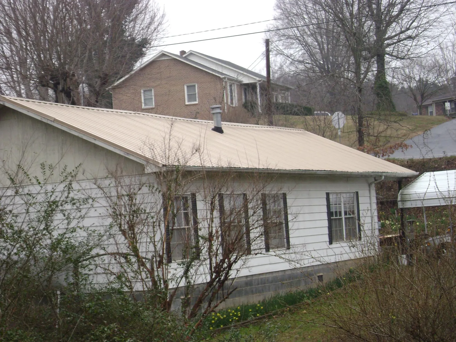 Tan metal roof on a white sided house set into a hillside — Commercial Roofing by Roofing Brothers in Inkom